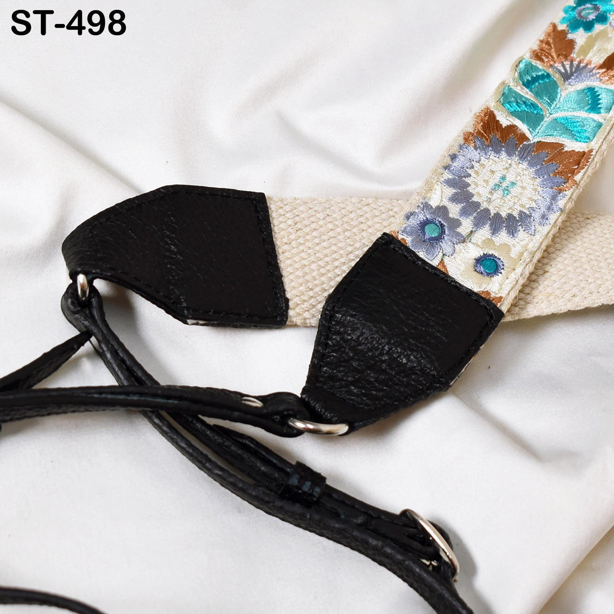 A close-up view of a black leather strap with a floral pattern, resting on a white fabric surface.