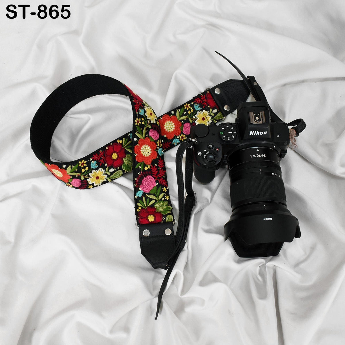 A floral-patterned camera strap and a Nikon camera are placed on a white fabric surface.