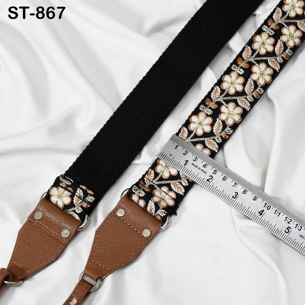 A black strap with a floral pattern and a brown leather strap are placed next to a ruler on a white background.