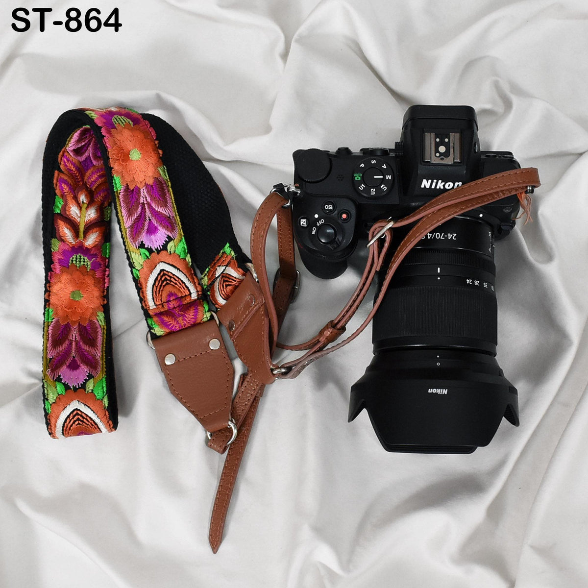 A black Nikon camera with a colorful floral patterned strap is placed on a white surface.