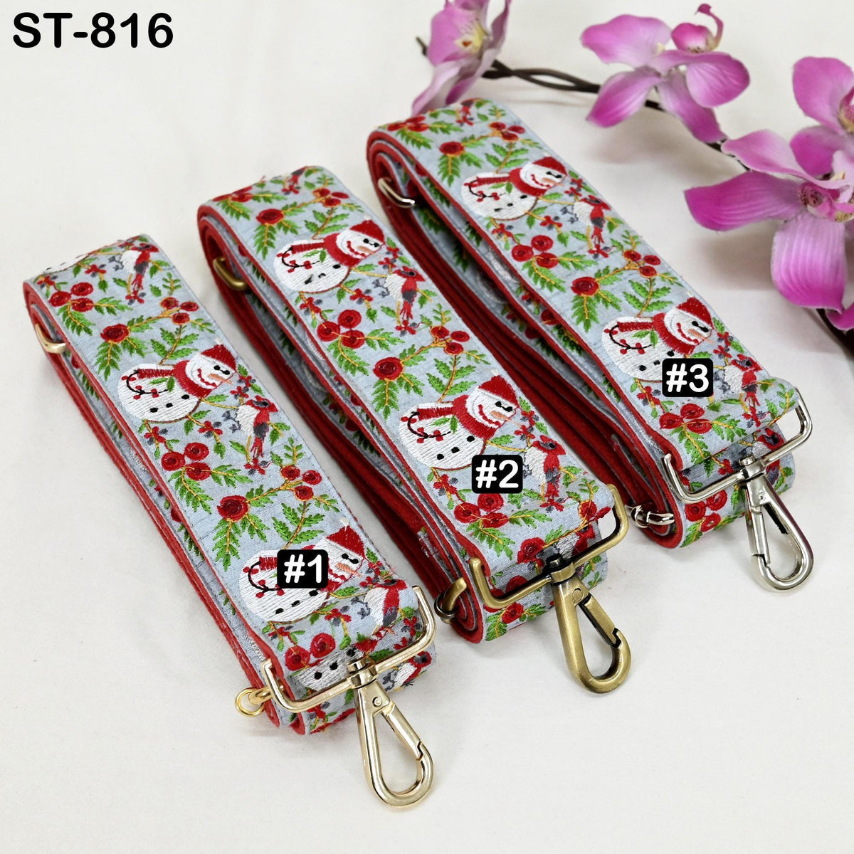 Three patterned straps with a floral design, each with a metal clasp and a small tag with a number printed on it. The straps are placed next to a branch of pink flowers.