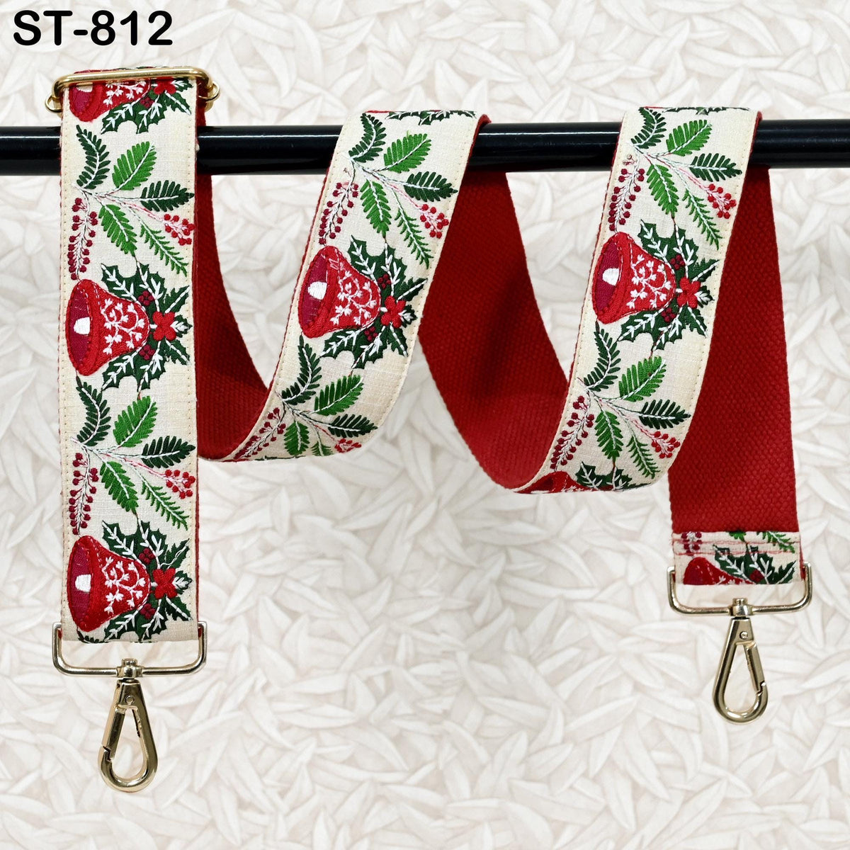 A red and white patterned fabric strap with a metal clasp and hook attached to a black metal bar.