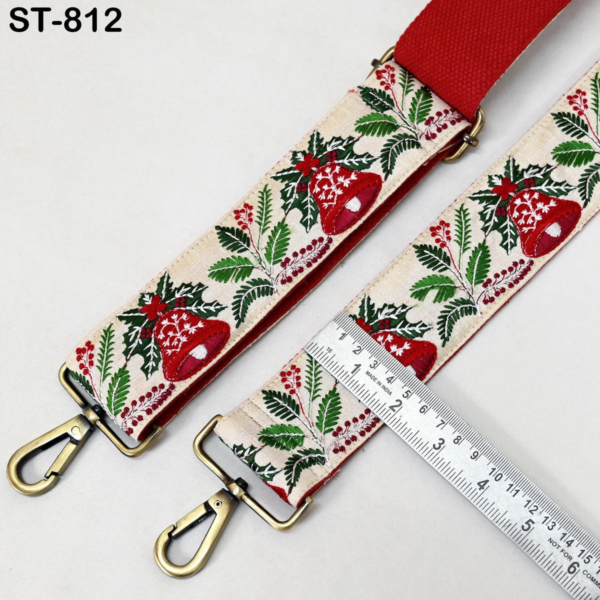A red and white patterned fabric strap with a metal clasp and a ruler for size comparison.