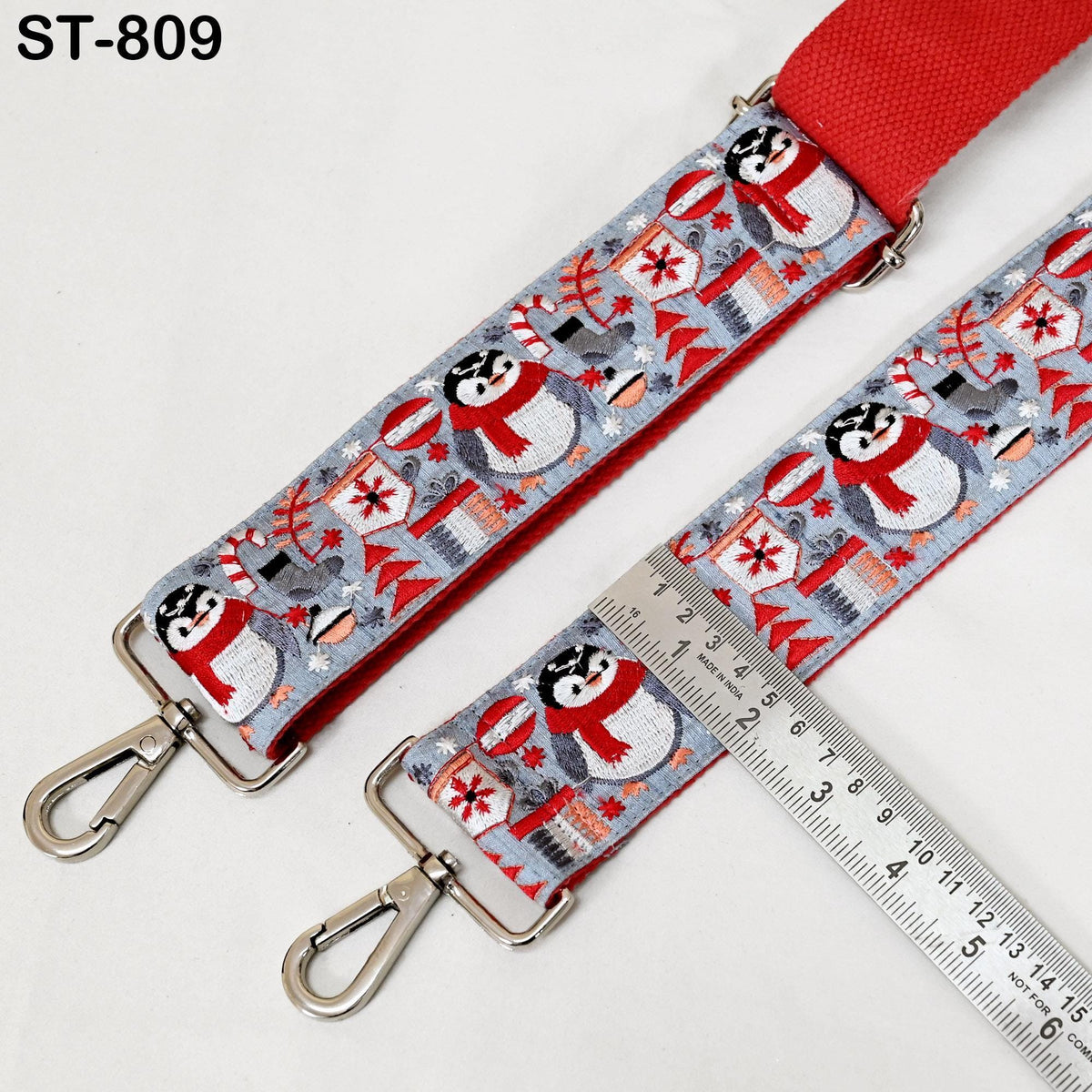 A red and gray patterned strap with penguin illustrations, and a metal ruler placed on top of it.