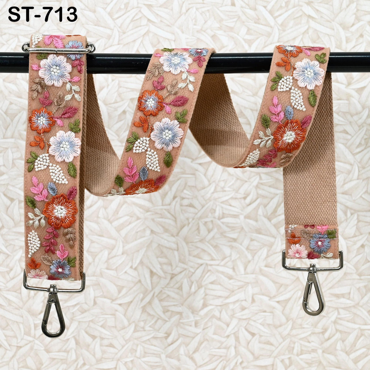 a floral-patterned beige strap with a metal hook attached to it, hanging on a black rod.