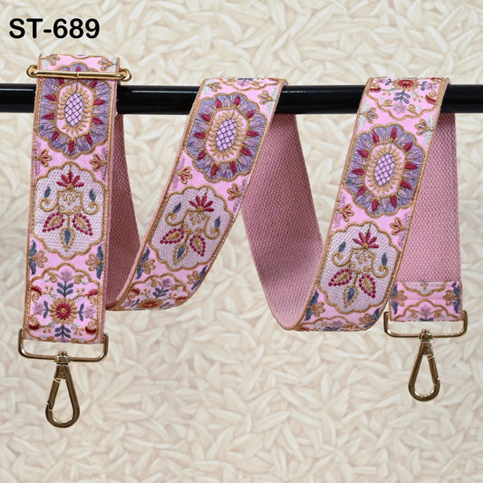 A pink floral embroidered strap with gold hardware, hanging on a black rod.