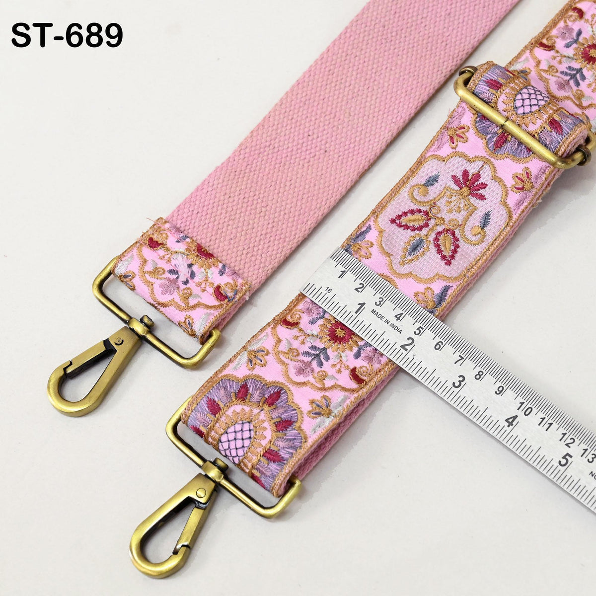 a pink strap with a floral pattern and a gold-colored metal buckle. The strap is being measured with a ruler, which is placed on a white surface.