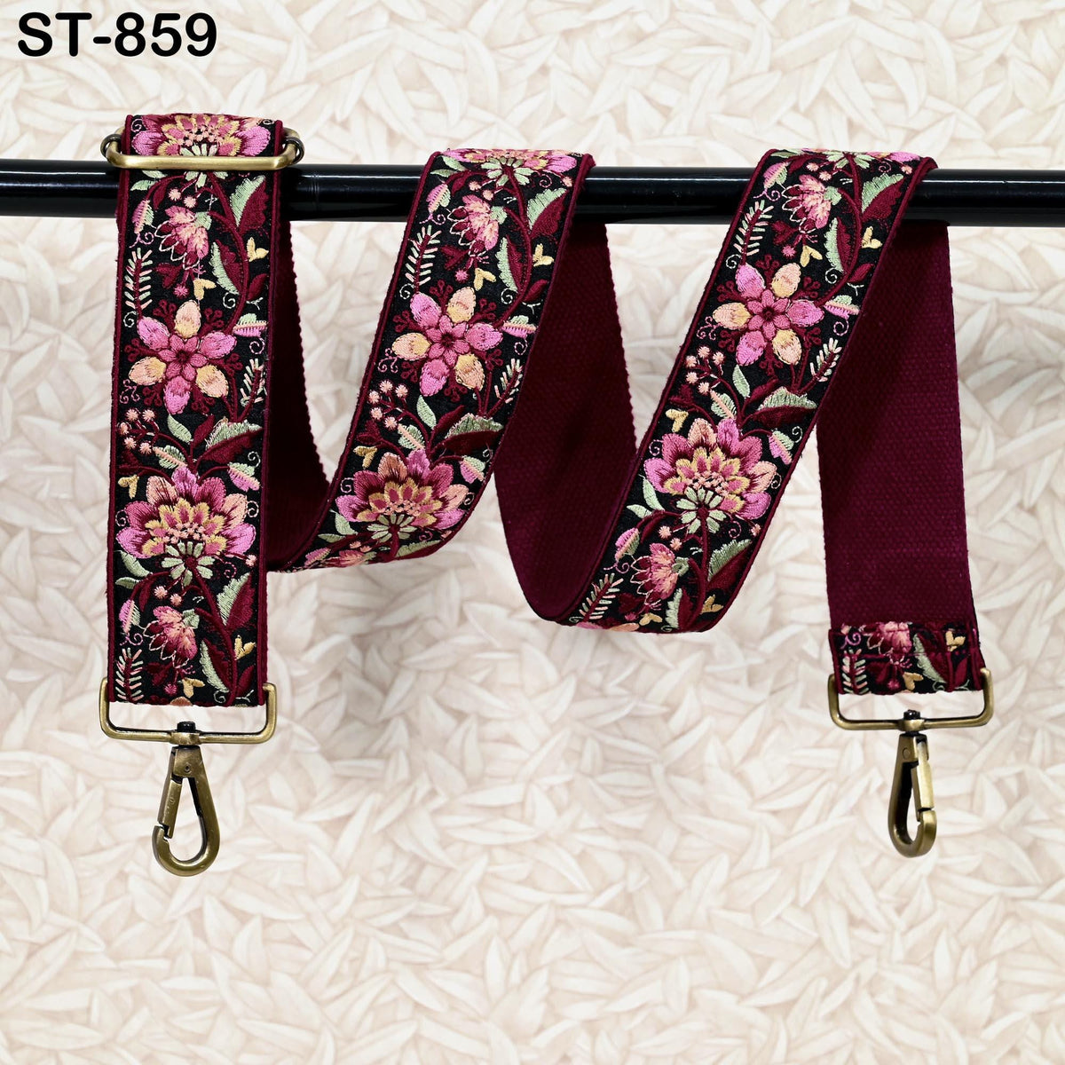 A floral embroidered strap with a clasp and hook attached, hanging on a black bar.
