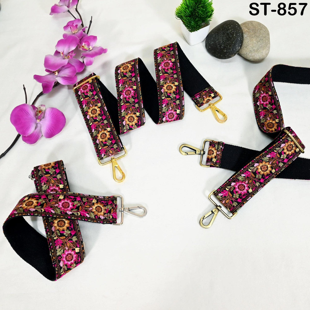 a collection of colorful floral straps, some of which are attached to a black strap, arranged on a white surface. There are also some rocks and purple orchids in the background.