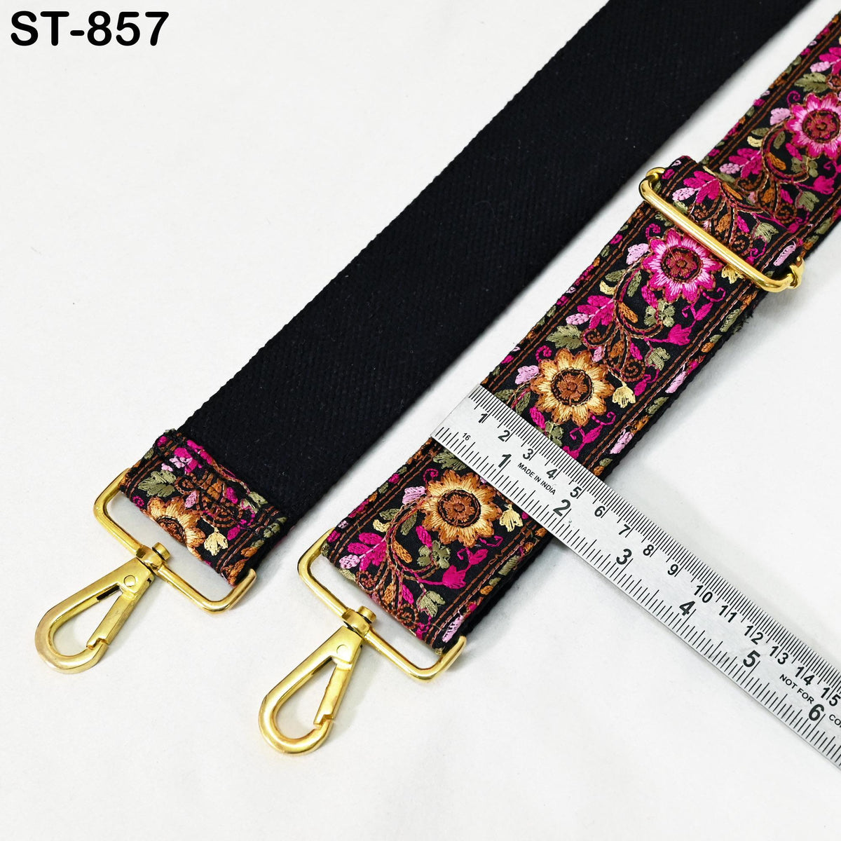 a black strap with a floral pattern and two gold metal hooks, accompanied by a ruler for size comparison.