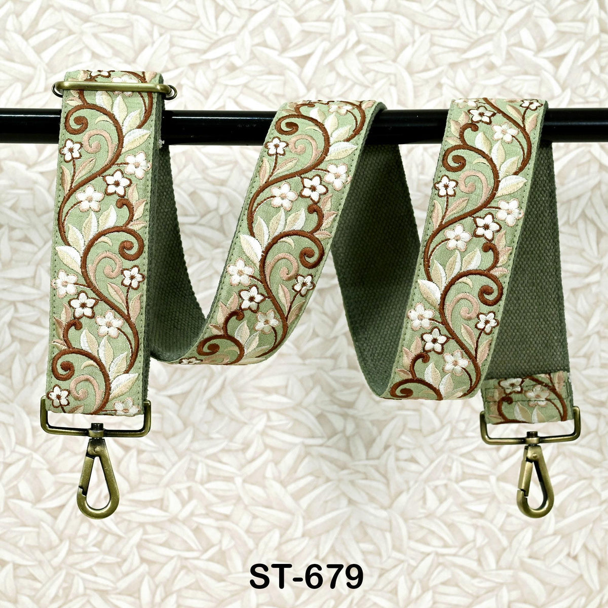 A green and white floral patterned strap with a metal clasp and hook attached to a black metal bar.