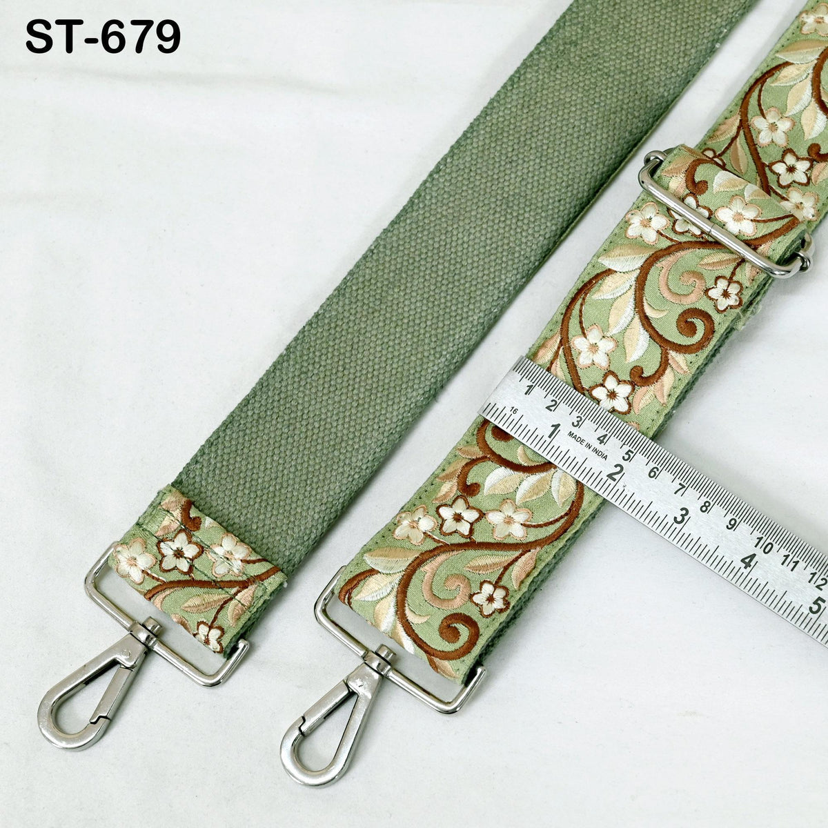 a green strap with a floral pattern and metal hooks, with a ruler placed next to it to measure the strap's length.