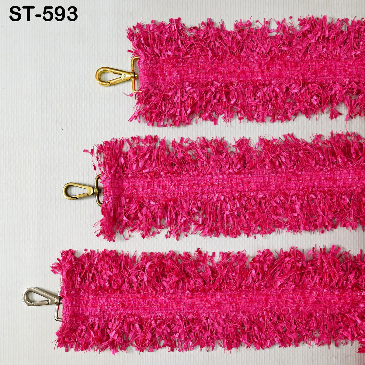 three pieces of pink, fuzzy fabric with a metallic gold hook attached to the top.
