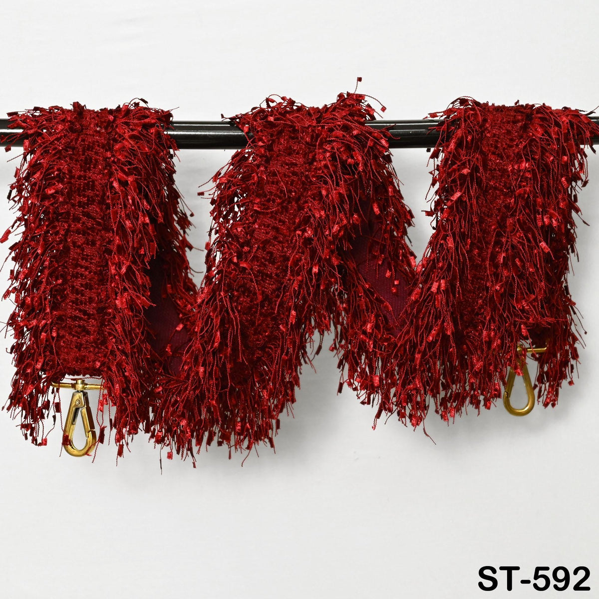 a red, fuzzy scarf with gold hooks hanging on a black rod.