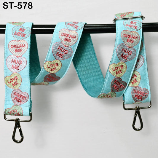 A blue strap with heart-shaped embroidered phrases such as "HUG ME", "DREAM BIG", "HUG ME", "LOVE ME", and "SWEET PEEL" printed on it.