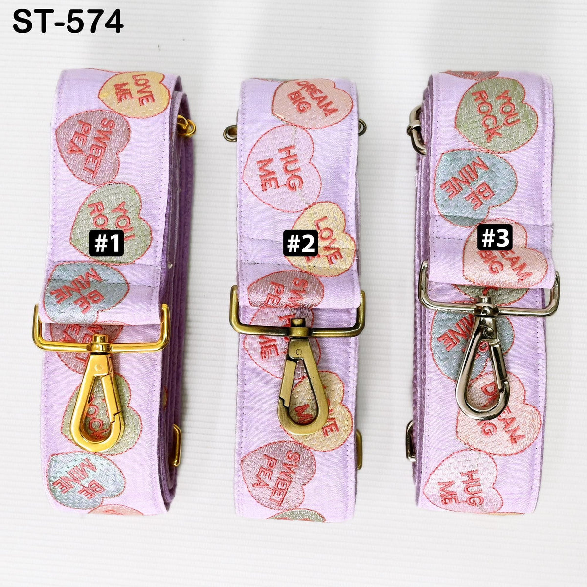 Three pink heart-shaped straps with the words "HUG ME" printed on them, each with a gold-colored metal clasp.