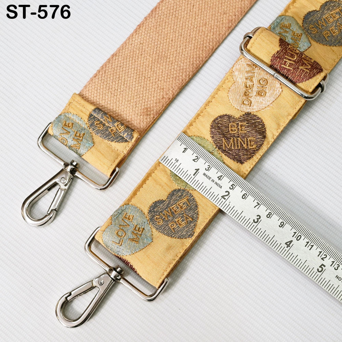 a beige strap with heart-shaped embroidered designs and a metal ruler placed on top of it.