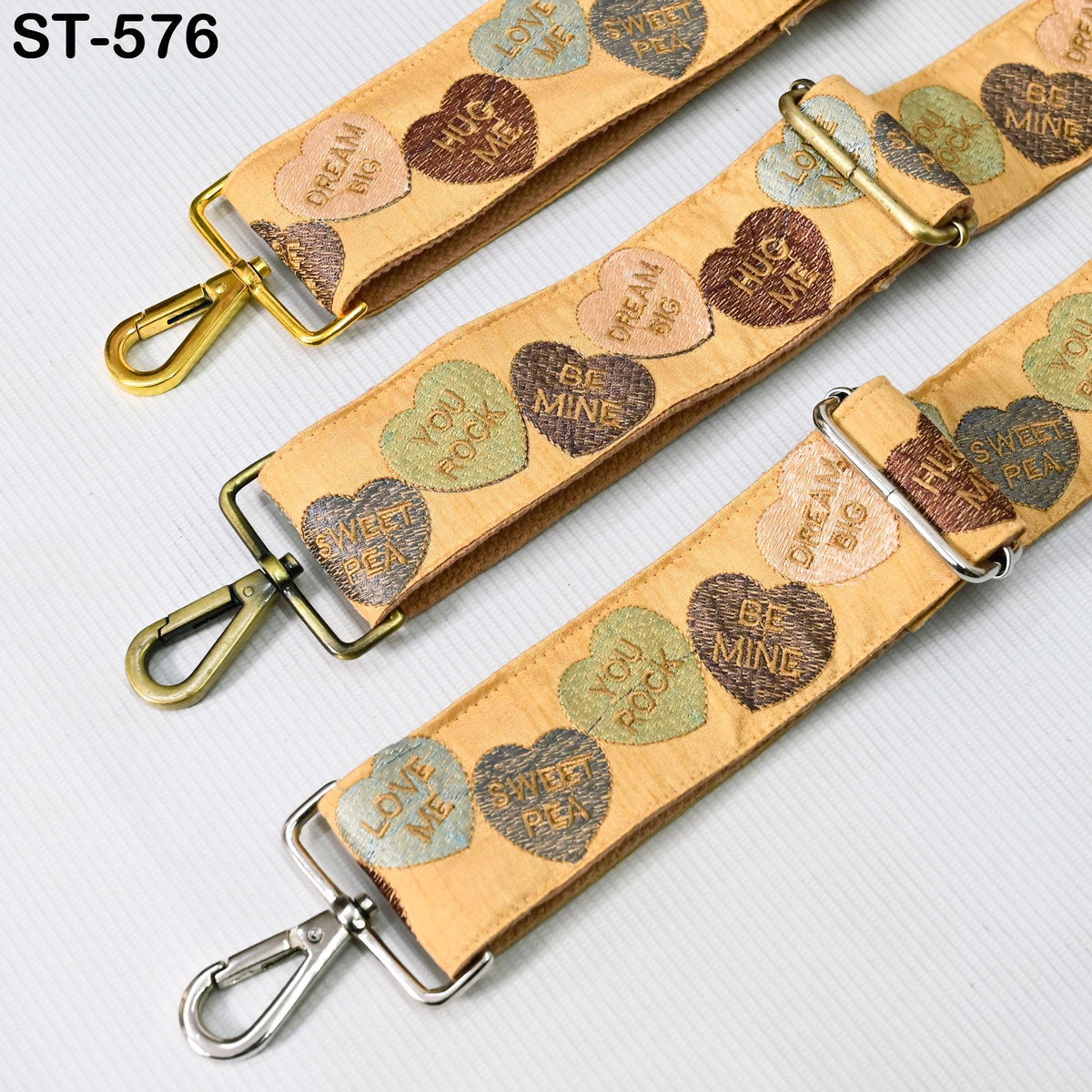 a collection of heart-shaped straps with various phrases printed on them, such as "Dream Big", "Be Mine", "Love Me", and "Sweet Pea". The straps appear to be made of a beige fabric and are attached to a metal clasp.