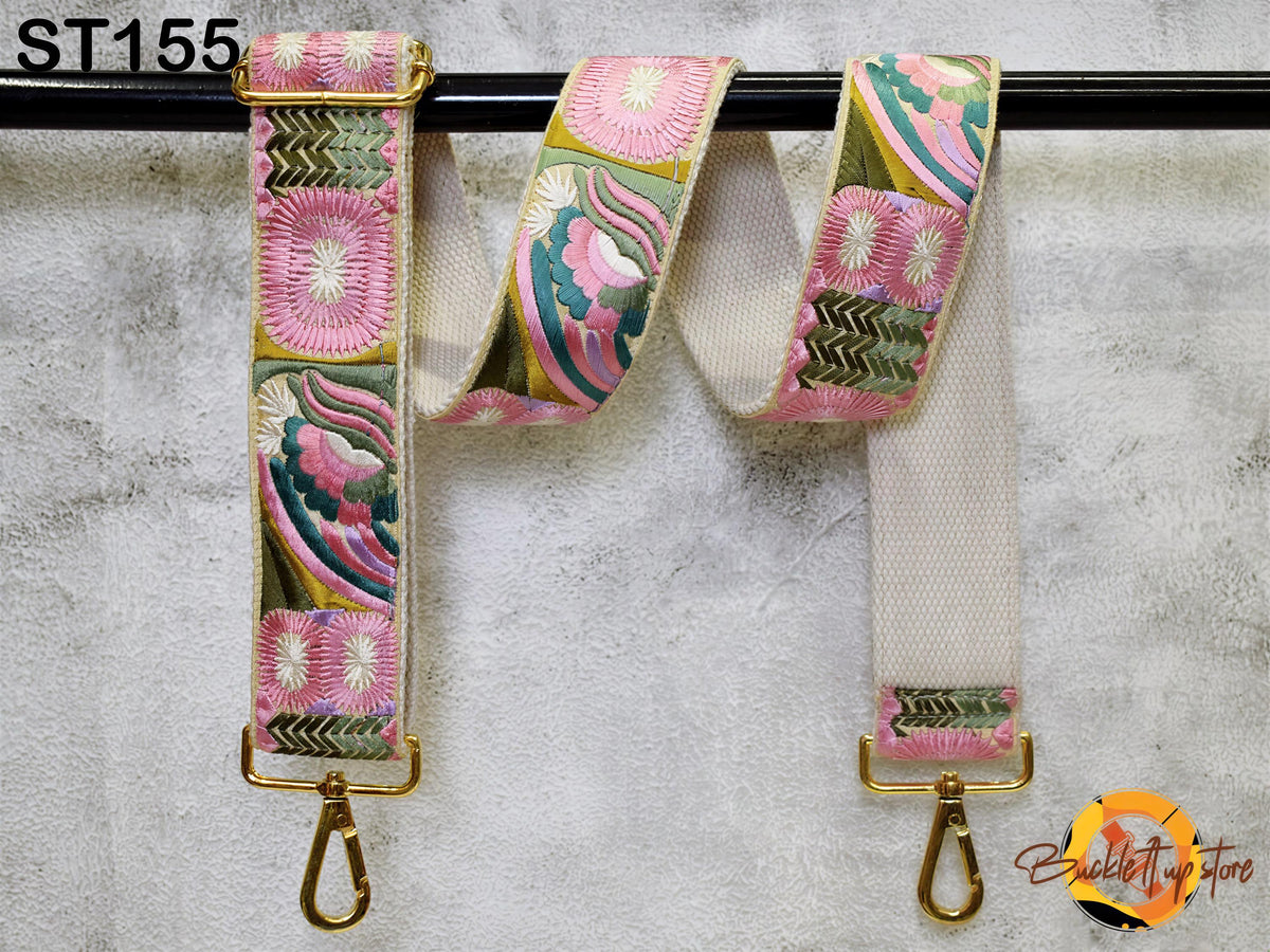 A colorful strap with floral patterns and a gold metal buckle, hanging on a black bar.