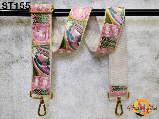 A colorful strap with floral patterns and a gold metal buckle, hanging on a black bar.