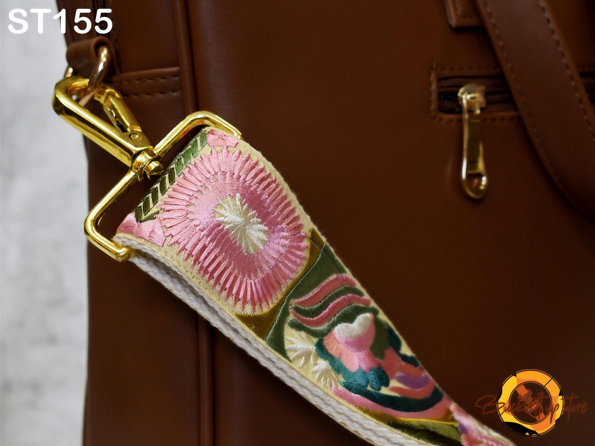 A close-up view of a brown leather bag with a gold metal zipper pull and a colorful strap featuring a floral pattern.