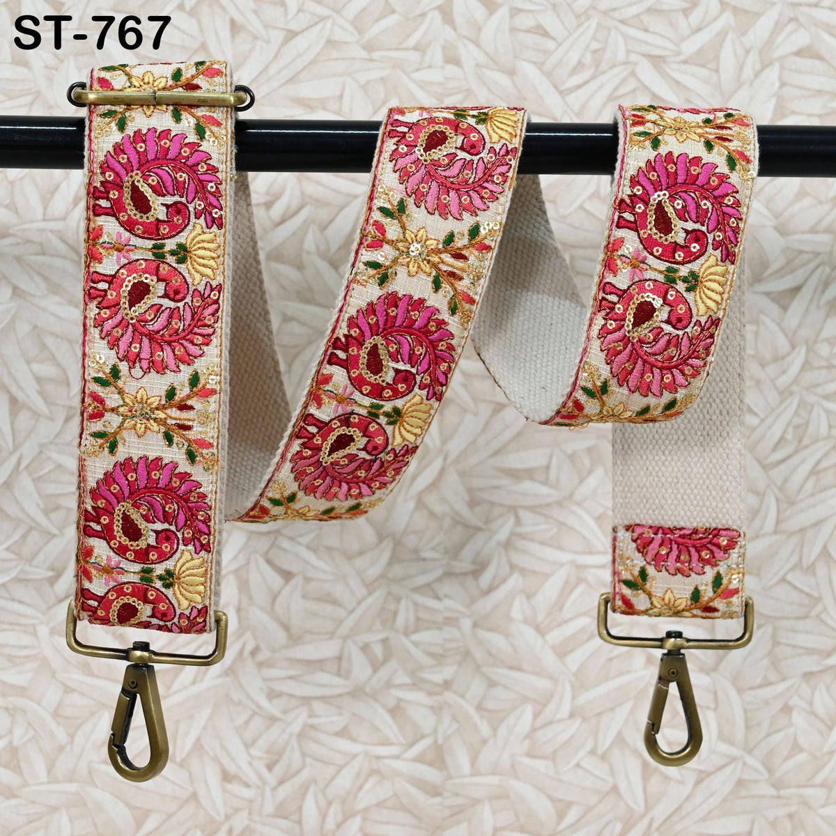 A decorative fabric strap with a floral pattern in pink and white colors, hanging on a black rod.