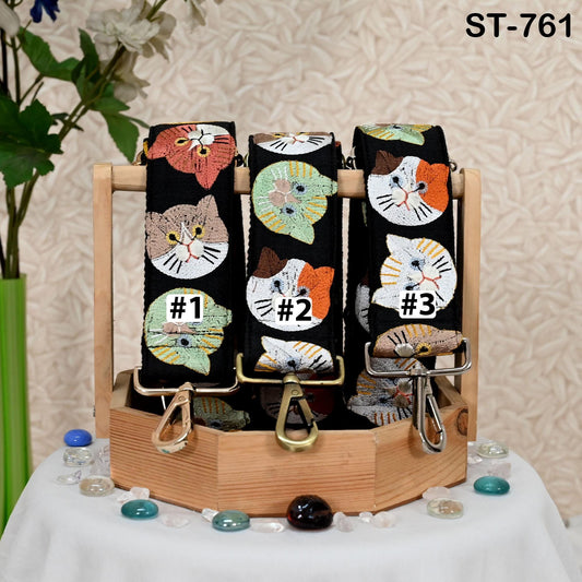 A display of three cat-themed straps, each with a unique design, arranged on a wooden stand.