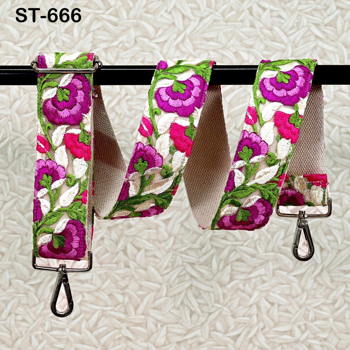 A floral-patterned strap with a metal hook attached, hanging on a black bar.