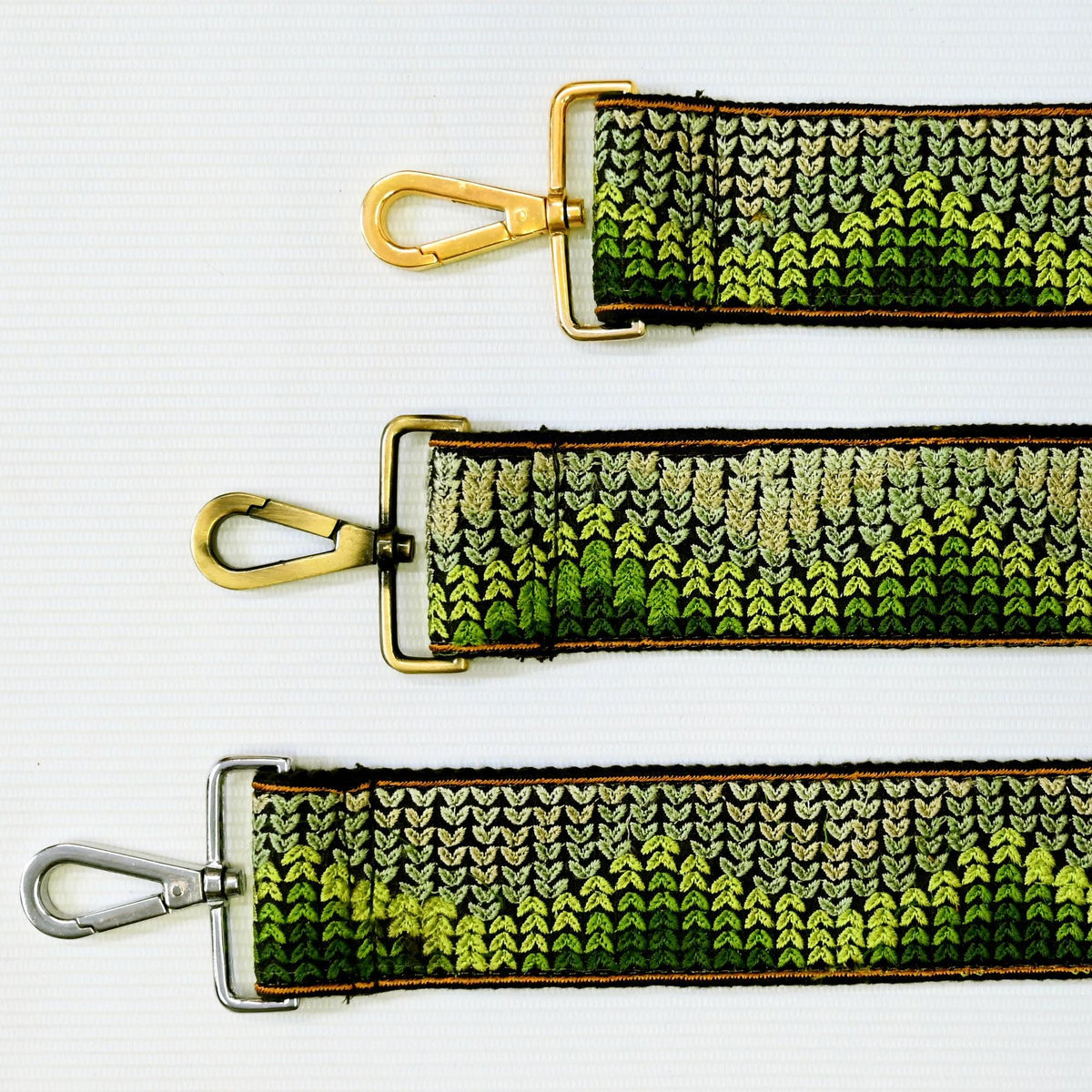 three different straps with a green and black knitted pattern. The straps appear to be made of a material that resembles a knitted fabric, with a metallic or metallic-looking clasp.