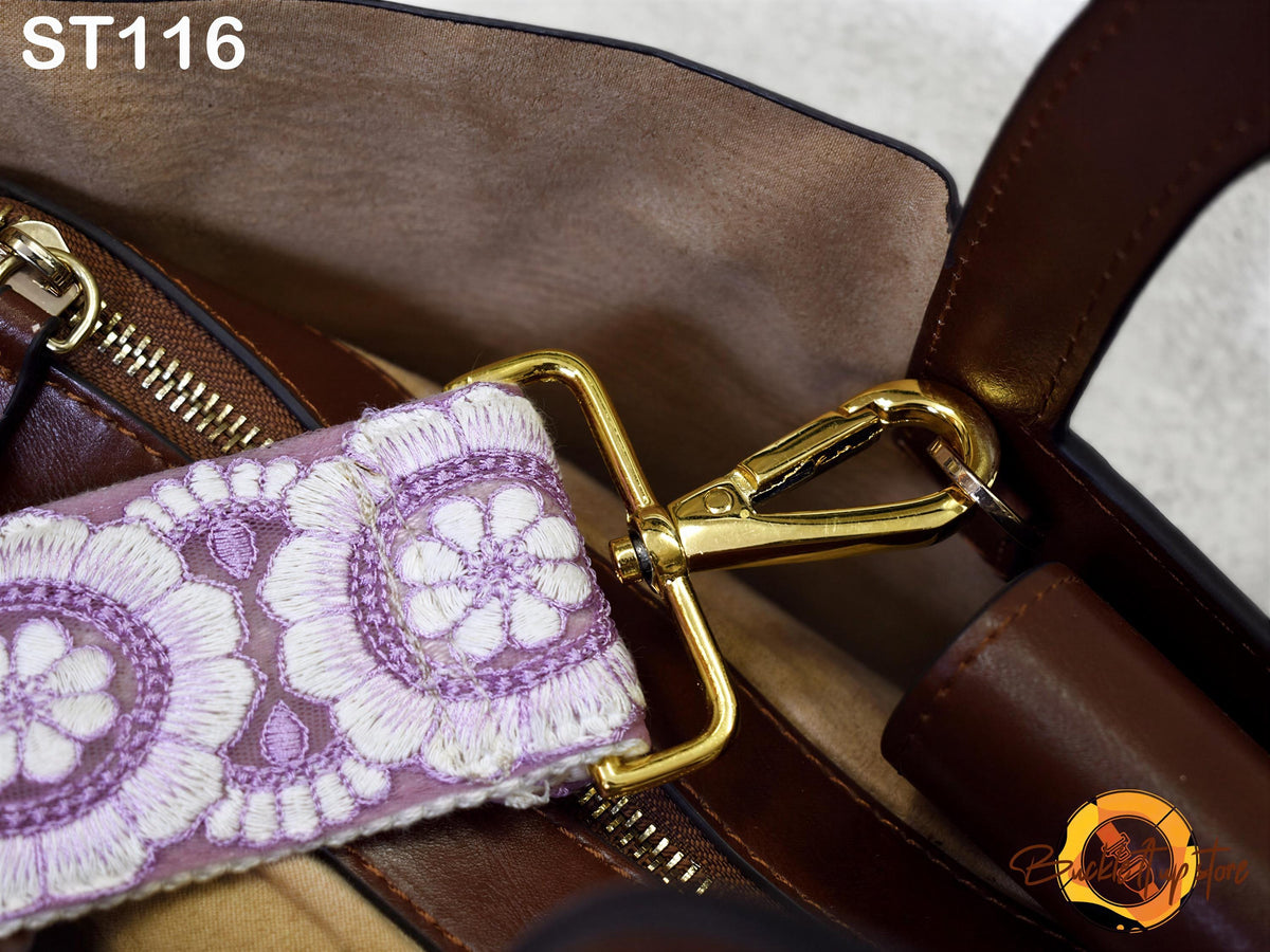 A close-up view of a brown leather handbag strap with a floral pattern, featuring a gold metal buckle.