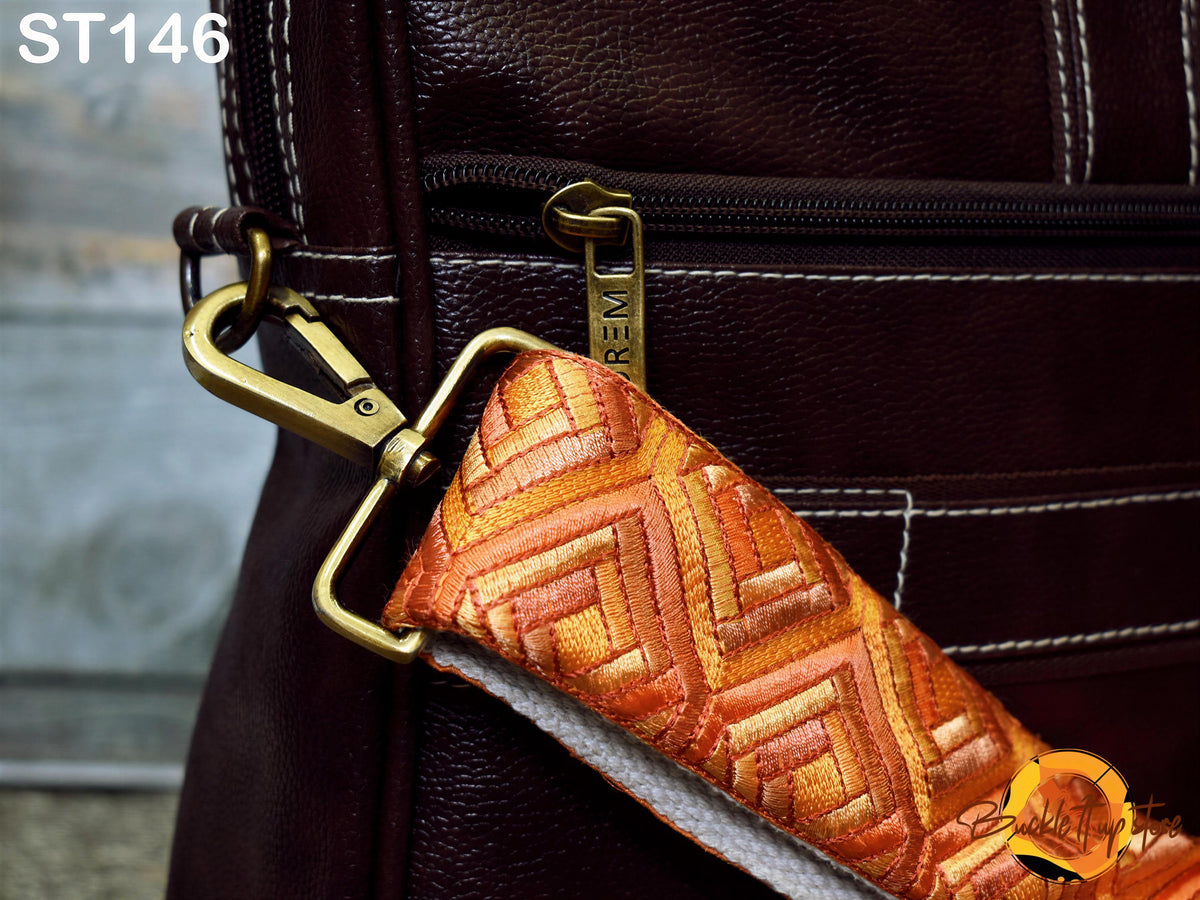 A close-up view of a brown leather bag with a gold zipper pull and a patterned strap.