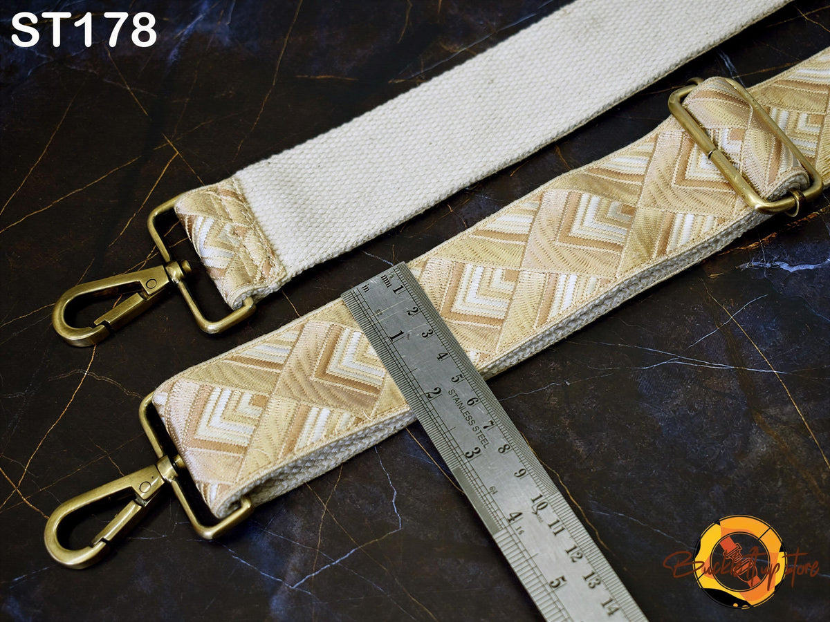 a white strap with a geometric pattern, a metal ruler, and a gold-colored metal clasp.