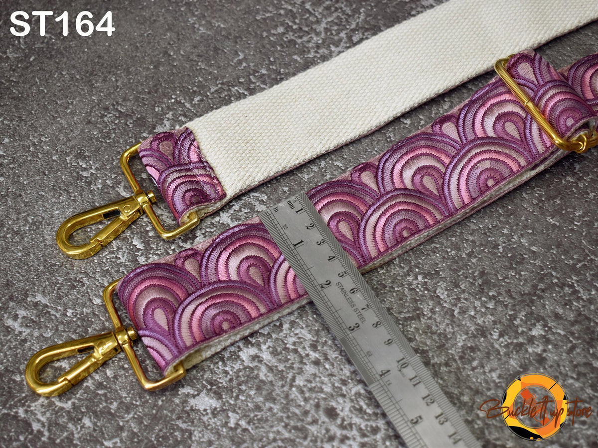 a strap with a pattern of purple and pink waves, and a ruler is placed next to it on a gray surface.