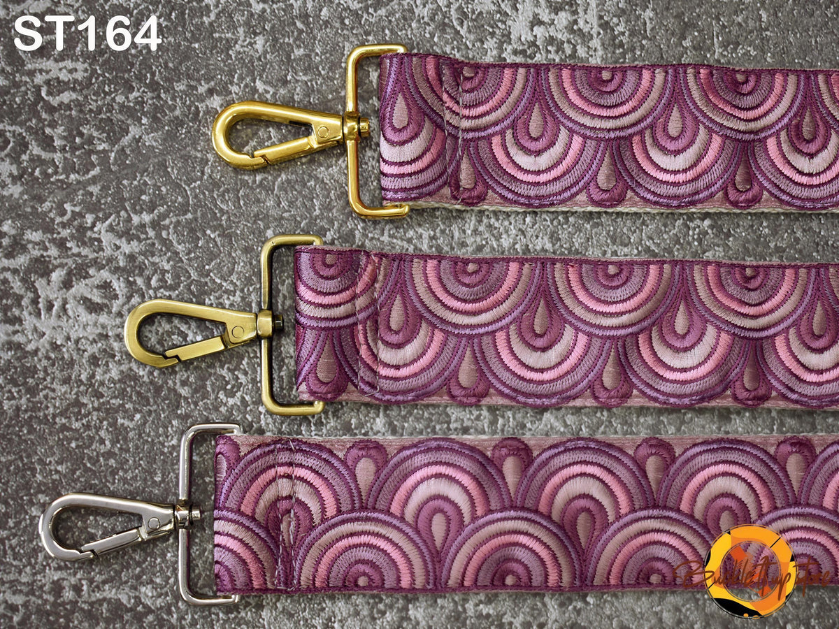 three straps with a repeating pattern of pink and purple waves. The straps have gold buckles and metal clips, and the straps are arranged in a row on a gray surface.