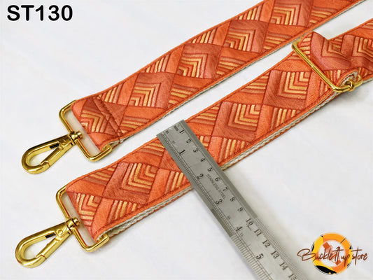 a pair of orange and gold patterned straps with a ruler placed between them, indicating the size or dimensions of the straps.