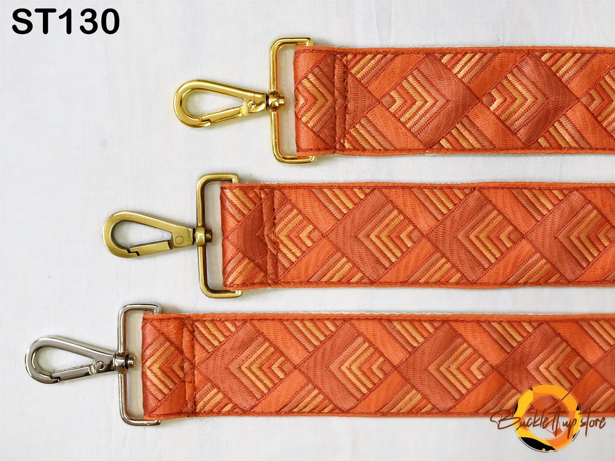 three different straps with a geometric pattern in shades of orange and gold. The straps appear to be made of fabric and have metal hardware, such as buckles and clasps.