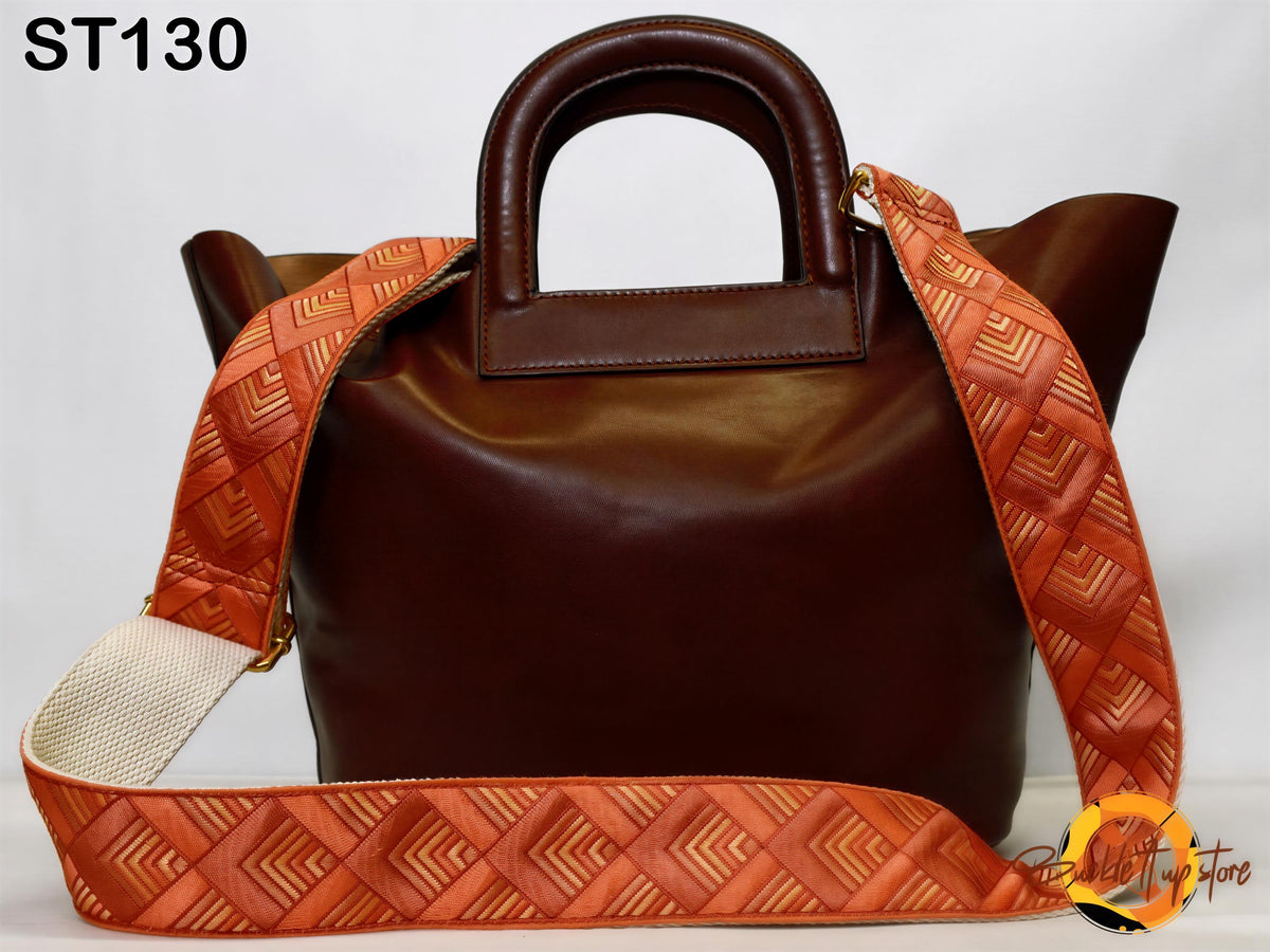 A brown leather handbag with a patterned orange strap, displayed against a white background.