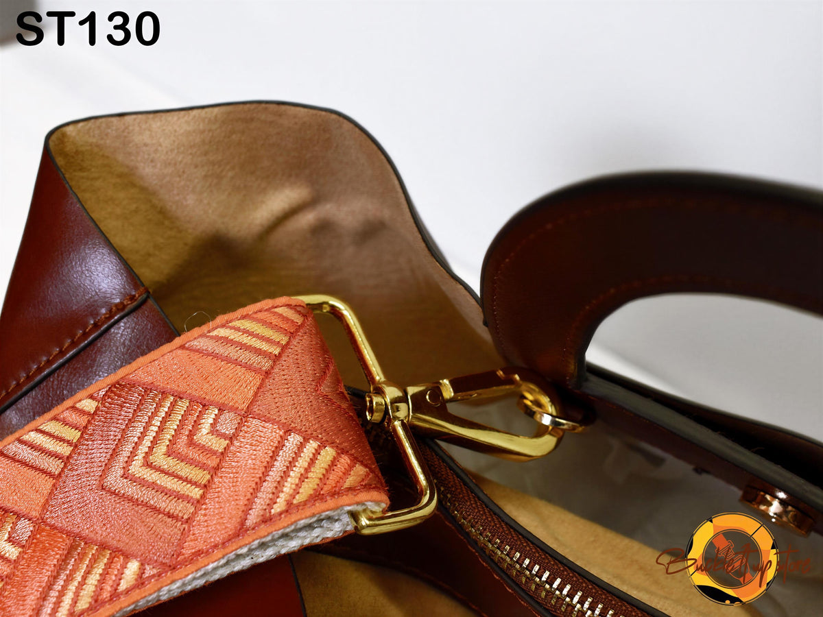 A close-up view of a brown leather handbag with a gold metal zipper pull and a patterned strap.
