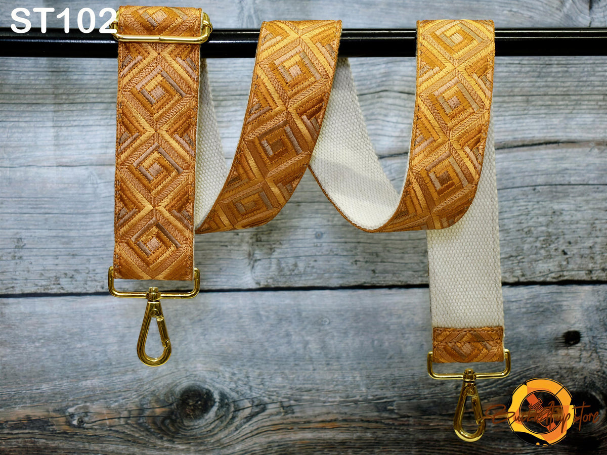 a pair of gold-colored straps with a geometric pattern, hanging on a wooden surface.