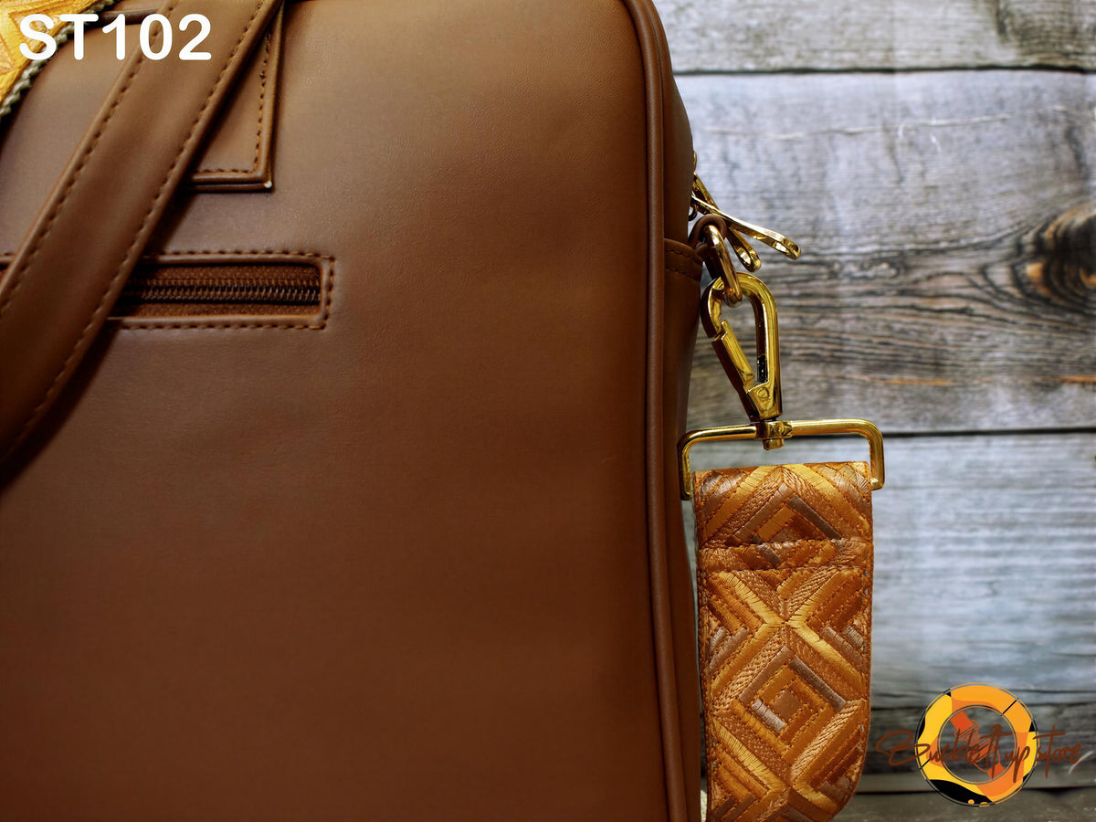 A close-up view of a brown leather bag with a gold metal zipper pull and a patterned strap, set against a wooden background.