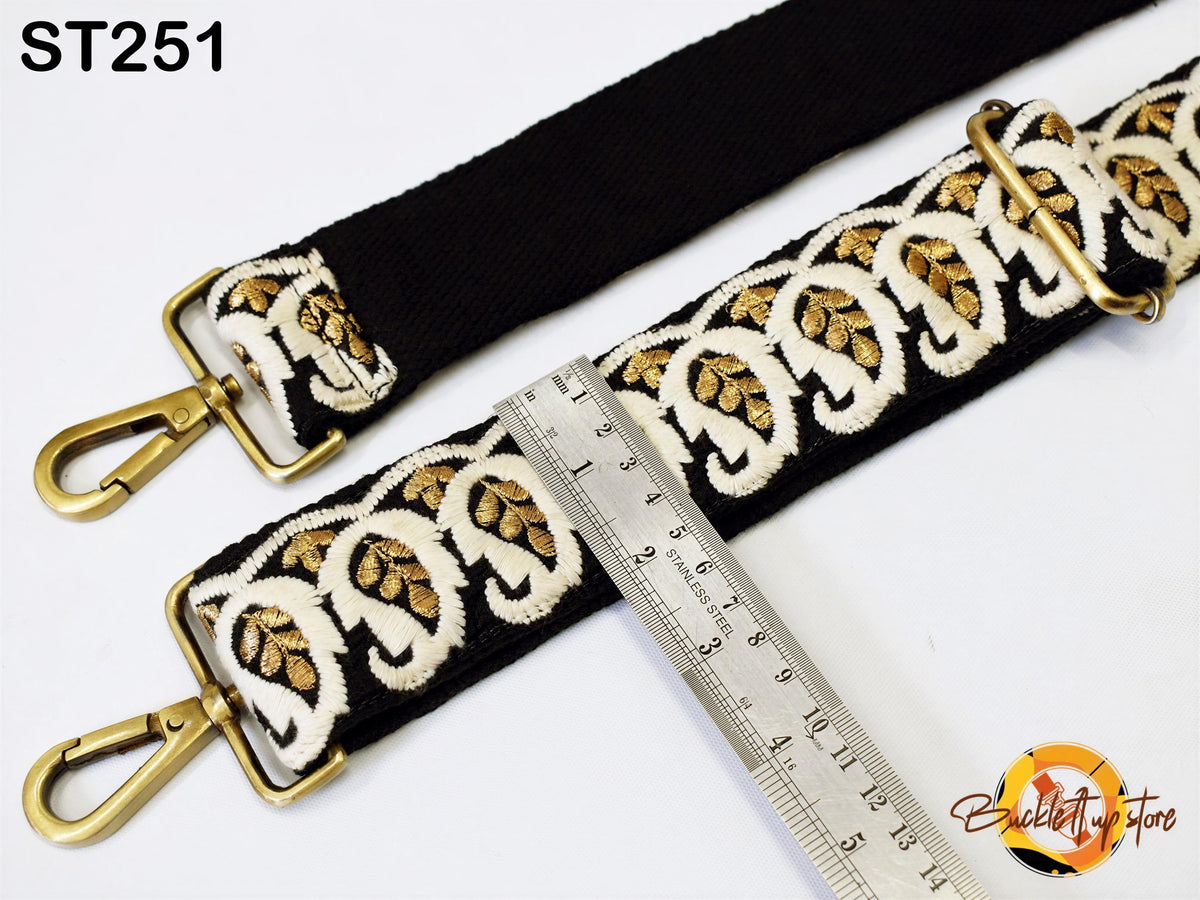 a black strap with gold embroidered designs, and a ruler is placed next to it, indicating the strap's length.