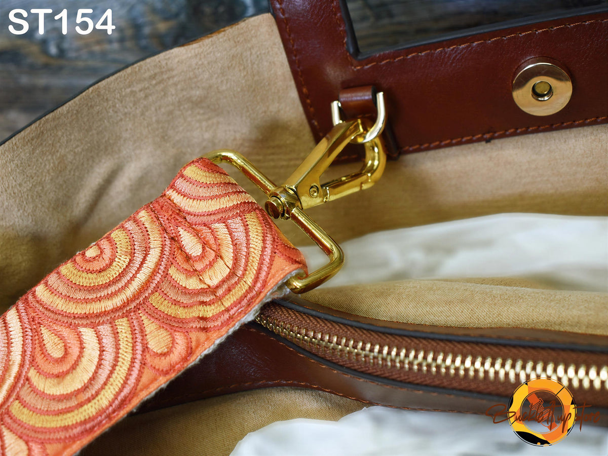 A close-up view of a brown leather handbag strap with a gold metal buckle, featuring a pattern of orange and yellow circles.