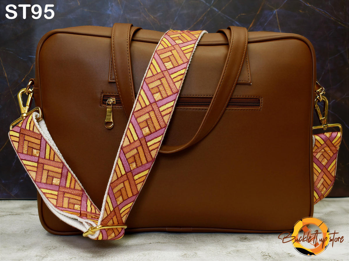 A brown leather laptop bag with a colorful patterned strap, placed on a surface against a dark background.