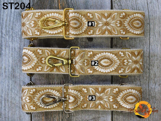 Three beige and gold floral straps with metal buckles are displayed on a wooden surface.