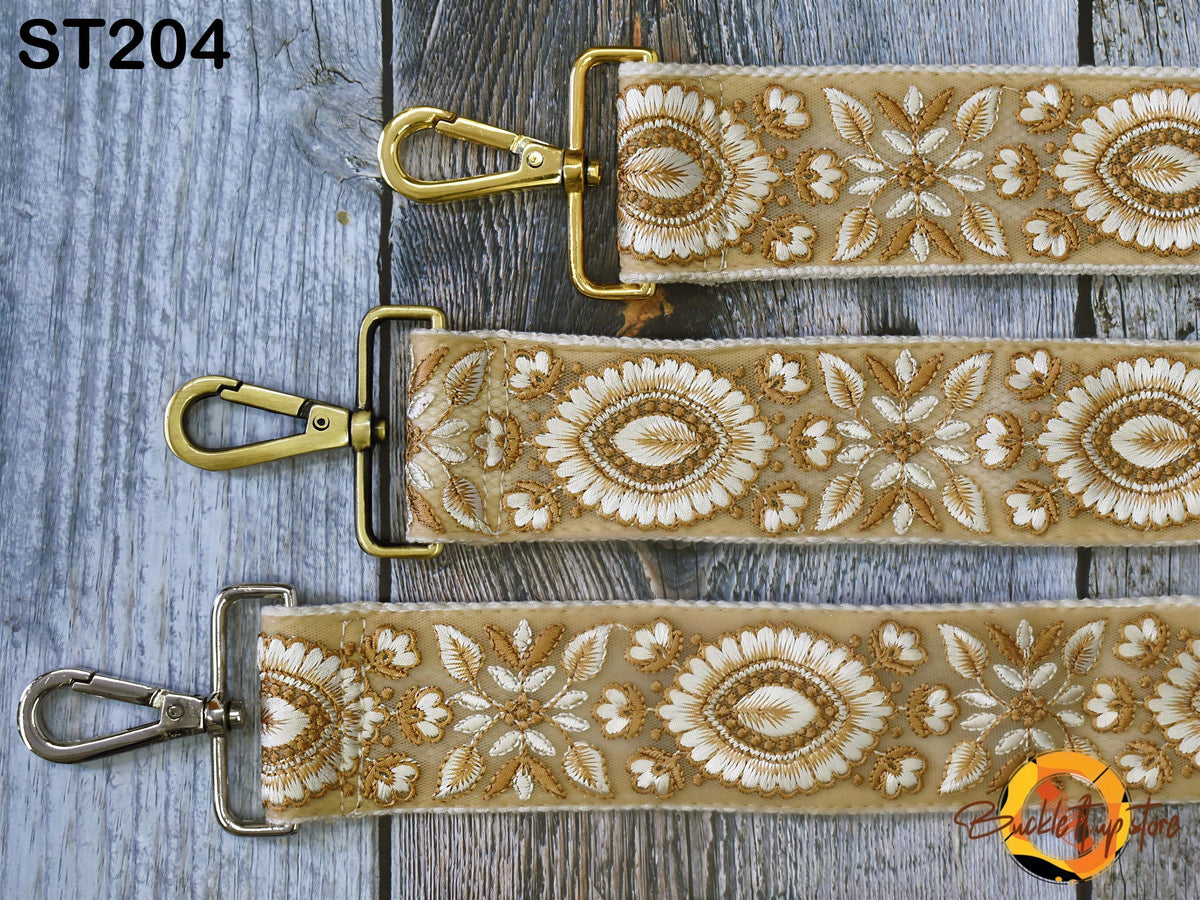 three straps with gold metal buckles and a floral pattern, arranged on a wooden surface.