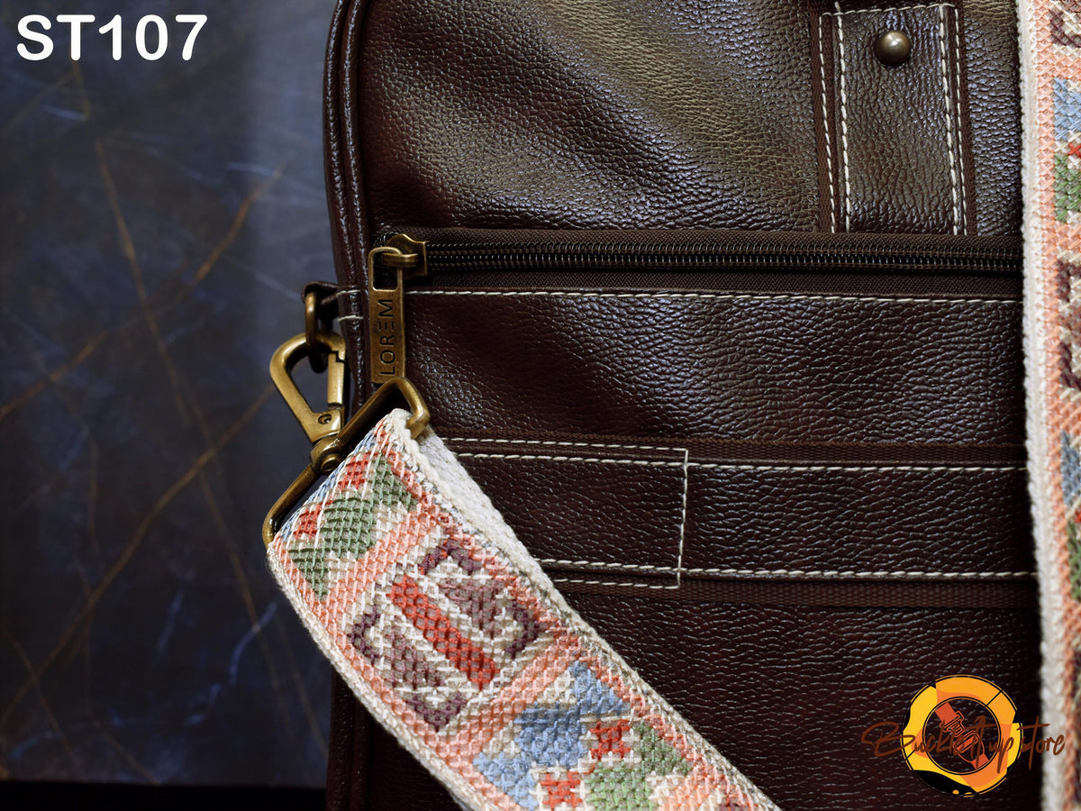 A close-up view of a brown leather bag with a colorful patterned strap, featuring a zipper closure and a metal clasp.