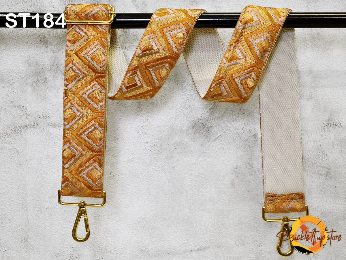 a gold-colored strap with a geometric pattern, hanging on a black bar.
