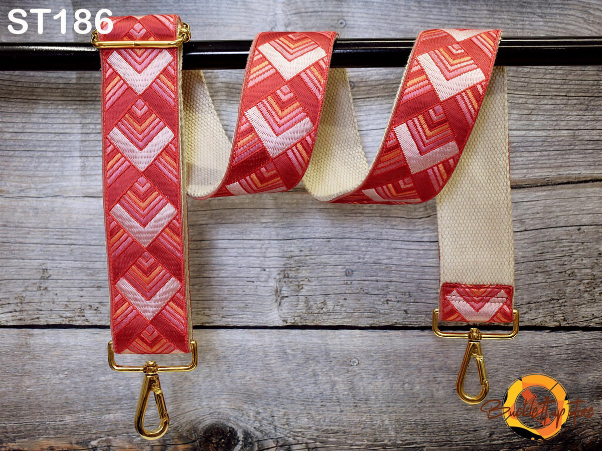 a red and white patterned strap with a gold metal buckle, hanging on a wooden surface.