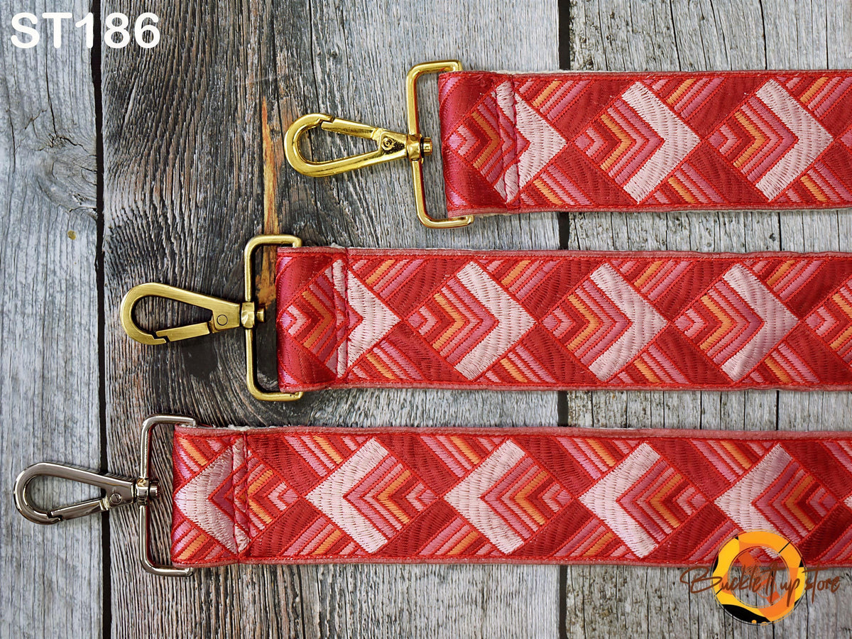 a set of three red and gold straps with a geometric pattern, laid out on a wooden surface.