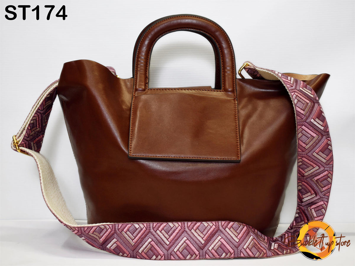 A brown leather handbag with a patterned strap, featuring a handle and a small pocket on the front.